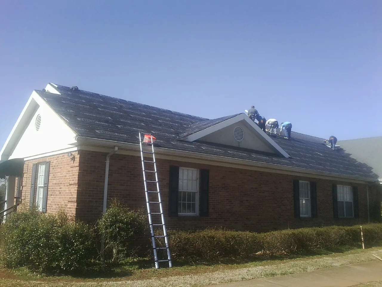 Crew tearing shingles off a brick ranch roof with a ladder set — Emergency Roof Repair work by our crew in Daleville
